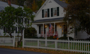white new england style home in the fall with orange leaves on the ground and pretty white wooden picket fence